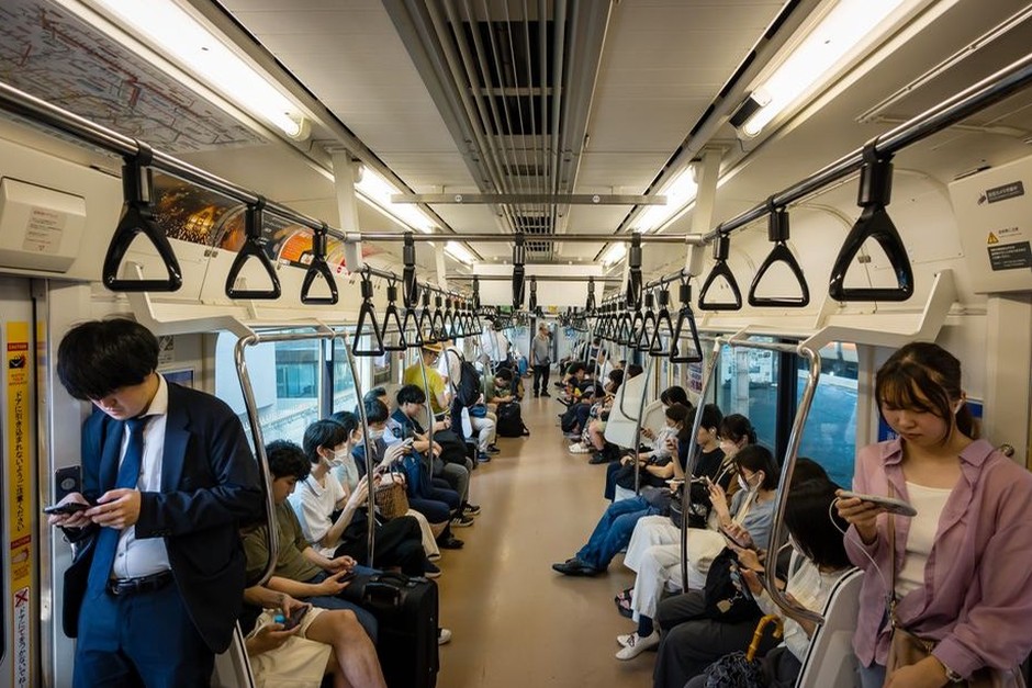 Commuters riding through a city in a bright train carriage.