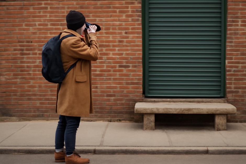 Person pausing on a sidewalk to photograph an ordinary urban detail